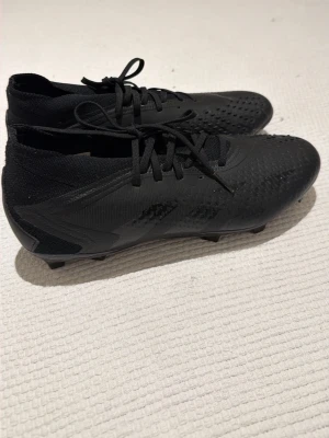 Svarta Adidas fotbollsskor - Säljer shelvinga svarta Adidas fotbollsskor med snörning och låg strumpliknande krage. Skorna har struktur på ovandelen för bättre bollkontroll och är tillverkade i syntetmaterial. Använd max fem gånger