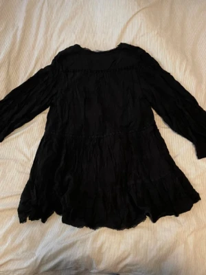 Svart klänning med volang - Svart kortklänning med v-ringning och volangdetaljer. Klänningen har långärmade ärmar och en luftig, flowy passform. 