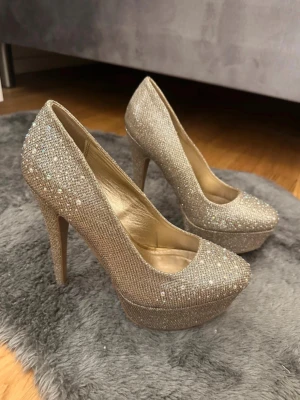 Glittriga guldfärgade klackar  - Säljer ett par glittriga guldfärgade klackar med hög klack och platåsula. Skorna är täckta av små gnistrande stenar som är jätte festliga🫶🏼🫶🏼