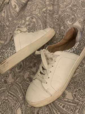 Vita sneakers med silverglitter - Säljer dessa vita skor med glitter häl från ONLY. Skorna är perfekta till sommar eller vår. Skorna har hål i sulan vid hälen och några smuts märken men annars är de bra. 