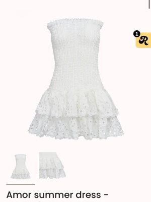 Vit volang favorittubklänning - Supersöt vit kortklänning med smockad överdel och dubbla volanglager i kjolen. Klänningen är axelbandslös och har broderade spetsdetaljer som ger en romantisk vibe. Perfekt för varma dagar och sommarhäng.