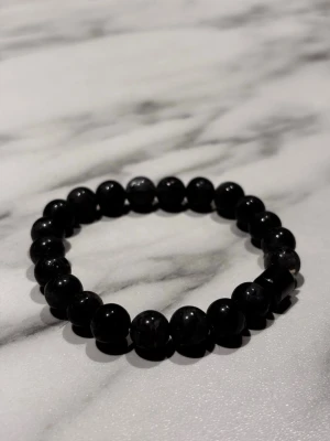Svart pärlarmband med elastisk tråd - Snyggt armband med Grå, runda pärlor trädda på elastisk tråd. Perfekt accessoar för dig som gillar en stilren och enkel look. Passar både till vardagsoutfits och mer dressade tillfällen. Inget synligt märke.
