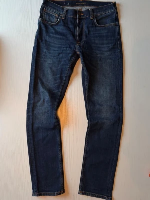 Mörkblå Lean Dean jeans från Nudie Jeans - Snygga mörkblå jeans från Nudie Jeans med klassisk femficksdesign i modellen Lean Dean i storlek 31/30 och slim tapered modell. Jeansen har precis varit inne på Nudie i Göteborg för förstärkning av grenen; se bild. Inte särskilt använda och lite snyggt inslitna och färgen heter Dark Deep Worn, något mörkare än på vissa bilder. Hojta för mått osv. OBS inga hål eller liknande.