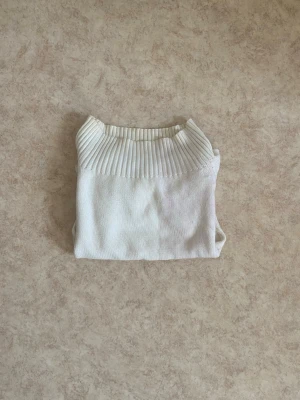 Vit stickad tröja med ribbad krage - Säljer en stilren vit stickad tröja med bred ribbad krage och ribbade detaljer vid midjan. Tröjan har en figurnära passform och långa ärmar. Perfekt att matcha med jeans för en clean look. Går även att använda som offshoulder topp då materialen kan stretcha bra :)
