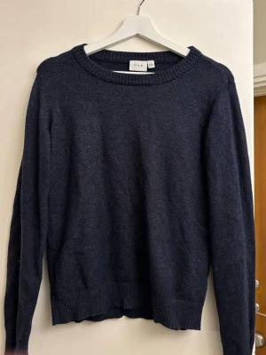 Mörkblå stickad tröja från Vila - Mysig mörkblå stickad tröja från Vila med rund halsringning och ribbade muddar vid ärmslut och nederkant. Perfekt för lager på lager och enkel att matcha med olika outfits. Klassisk och stilren design. 