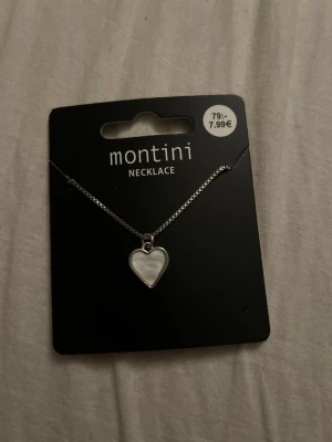 Halsband med hjärthänge från Montini - Snyggt halsband från Montini med ett silverfärgat kedja och ett hjärtformat hänge i pärlemor-look. Perfekt accessoar för att lyfta din outfit med en söt och stilren detalj. Hjärtat ger en romantisk touch och kedjan är tunn och elegant.