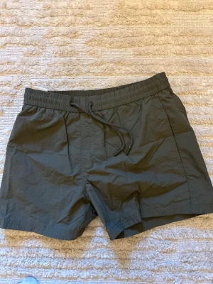 Mörkgröna badbyxor från Zara - Snygga mörkgröna badbyxor sopass kort modell från Zara. De har until resår i midjan med dragsko och innerbyxa i mesh. Perfekta för finalen på stranden eller poolhänget. Materialet är snabbtorkande syntet.