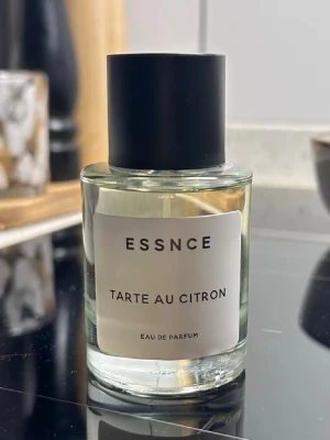 ESSNCE Tarte au Citron parfym length - Fräsch parfym från ESSNCE med doft av citronpaj. Flaskan är cylindrisk i genomskinligt glas Lambert med  svart matt kork och enkel vit etikett med svart text. Eau de Parfum som ger en fräsch wholesale och citrusaktig känsla.