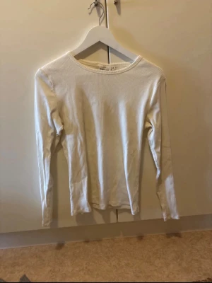 Vit ribbad långärmad topp - En enkel och stilren vit långärmad topp med ribbad struktur. Toppen har rund halsringning och är figurnära i modellen, perfekt att matcha med jeans eller kjol. Materialet känns mjukt och stretchigt.