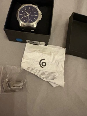 Silverfärgad klocka från Regal - Stilren klocka från Regal med silverfärgat metallarmband och mörkblå urtavla. Klockan har kronograf-detaljer och tydliga markeringar. Levereras i originalask med extra länkar för justering. Använd endast en gång. Priset kan diskuteras vid snabb affär. Nypris 500kr.