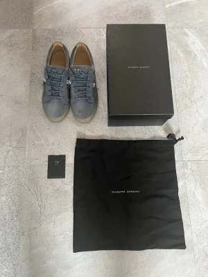 Blå sneakers från Giuseppe Zanotti - Snygga blå/ljusgrå sneakers i mocka från Giuseppe Zanotti med dragkedja och snörning. Skorna har en stilren design med en ljus sula och är perfekta för en trendig look. Hör av dig för mer info och undringar. Bra skick