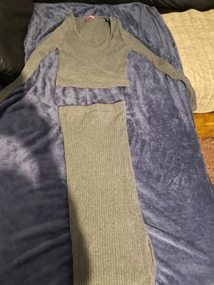 Grå ribbat set med långärmad topp - Säljer ett grått ribbat set med långärmad croppad topp och matchande höga byxor. Setet har en mjuk och stretchig känsla, perfekt för en avslappnad men ändå snygg look. Materialet är troligtvis en bomulls- eller viskosmix. Inga synliga loggor eller märken.