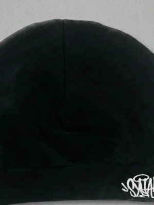 Svart mössa med broderad logga - Säljer en svart mössa i mjukt tyg med en vit broderad logga i graffiti-stil på kanten. Enkel och stilren design som passar till det mesta. Perfekt accessoar för kalla dagar.