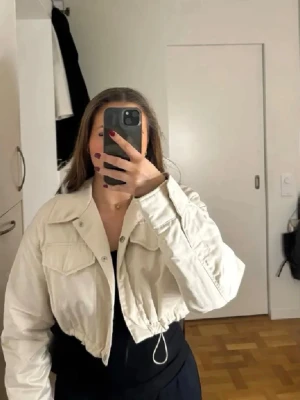 Bomberjacka - Snygg beige/cremefärgad croppad jacka från Zara. Den har två fickor framtill och går att spänna till längst ner beroende på hur tajt man önskar att den sitter. Använd fåtal gånger!  