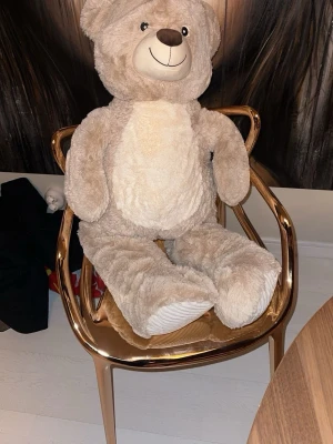 Stor beige nallebjörn - Mysig och stor nallebjörn i beige plysch med vit mage och tassar. Nallen har ett glatt ansikte med broderad nos och ögon. Perfekt som dekoration eller kramkompis i rummet.