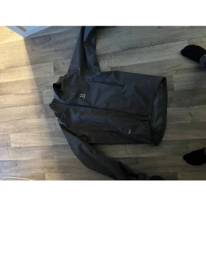 grp regnjacka från Haglöfs - Säljer en svart regnjacka från Haglöfs med hel dragkedja och hög krage. Jackan har en justerbar huva och är tillverkad i ett vattenavvisande material. Perfekt för regniga dagar och outdoor-aktiviteter.