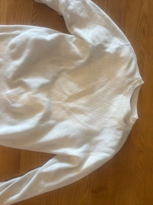 Vit tröja från Pull&Bear - Säljer en stilren vit tröja från Pull&Bear i storlek M. Tröjan har rund halsringning och är tillverkad i ett mjukt, strukturerat material med ribbade muddar vid halsen. Perfekt för en clean och enkel look.