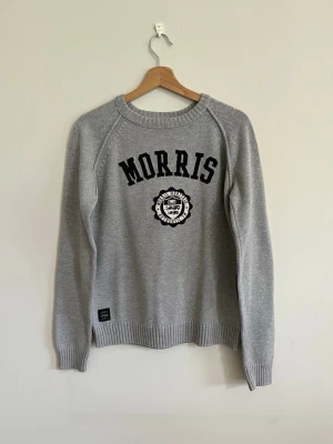 Grå tröja från Morris - Snygg grå tröja från Morris med svart text och emblem på bröstet. Tröjan har rund halsringning, långa ärmar och ribbade muddar vid ärmslut och nederkant. Perfekt för en avslappnad och stilren look.