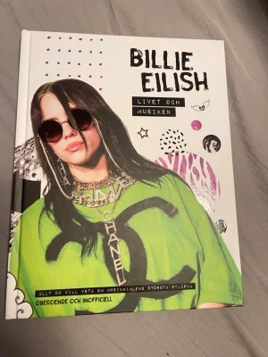 Billie Eilish: Livet och musiken - En färgstark bok om Billie Eilish med hård pärm och coolt grafiskt omslag i vitt, grönt och svart. Boken är fylld med bilder, fakta och berättelser om Billies resa till att bli en av världens största popstjärnor. Perfekt för dig som vill veta allt om musikikonen.