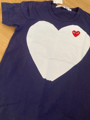 Mörkblå Comme des Garçons Play t-shirt - Snygg mörkblå t-shirt från Comme des Garçons Play med stort vitt hjärta på bröstet och det ikoniska röda hjärtat med ögon broderat. T-shirten har rund hals och är tillverkad i mjuk bomull. Perfekt för dig som gillar streetstyle och unika prints. Hör av dig vid minsta fråga 💖💖