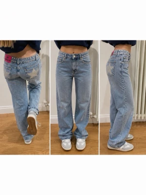 One Dilemma jeans med stjärnor & nitar - Blå jeans från One Dilemma med raka ben, silverfärgade nitar i midjan och längs bensluten samt glittriga stjärnor på bakfickorna. Tuff rosa patch bak i midjan. Perfekta för dig som vill sticka ut med coola detaljer och unik look.