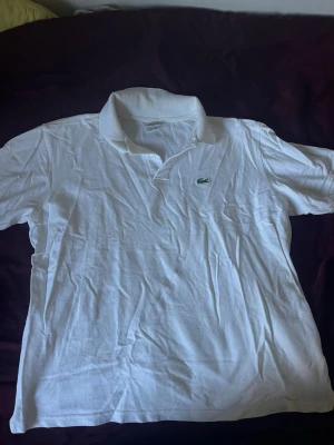 Vit pikétröja från Lacoste - Klassisk vit pikétröja från Lacoste med broderad grön krokodil på bröstet. Storlek L