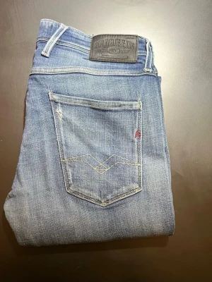 Blå Replay Anbass jeans - Storlek 33/32i slim. Jätte fint skick. Säljer ett par blå Replay Anbass jeans med snyggt slitna detaljer och klassisk femficksdesign. Jeansen har normal passform och raka ben, perfekt för en avslappnad stil. Märkeslapp bak i midjan och dragkedjegylf. Nya 2300. Priset får vi diskutera.