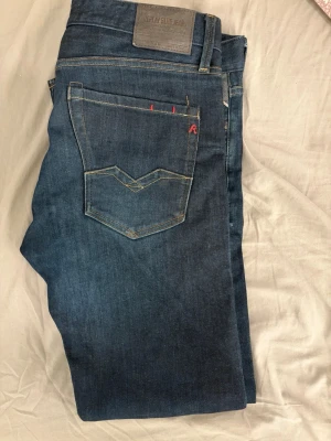Mörkblå Replay jeans med kontrastsömmar - Snygga mörkblå jeans från Replay med klassisk femficksmodell och kontrastsömmar. Bakfickorna har dekorativa sömmar och en liten röd detalj. Jeansen har en rak passform och är tillverkade i mjukt denimtyg.