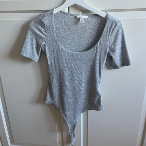 Grå body  - Säljer en grå ribbad bodysuit från H&M med rundad urringning och korta ärmar. Använt bara några få gånger, inga defekter eller något!! Som ny!🥰