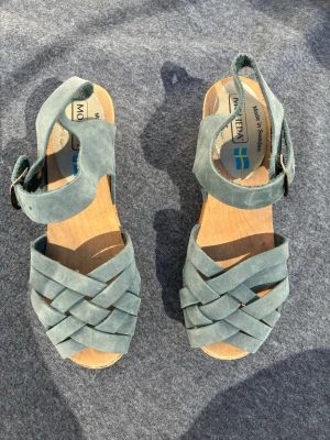 Blåa träskosandaler från Moheda - Snygga blåa sandaler från Moheda med klassisk flätad design i mocka och träfotsula. Justerbart spänne vid ankeln och öppen tå. Tillverkade i Sverige och perfekta för en chill sommarstil.