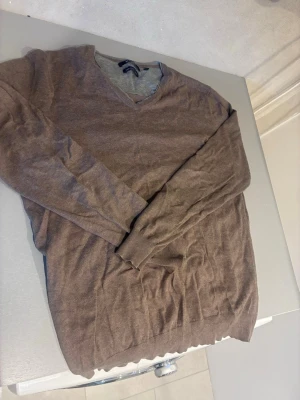 Brun V-ringad stickad tröja - Säljer en brun stickad tröja från Brothers med V-ringning och långa ärmar. Tröjan har ribbade muddar vid ärmslut och nederkant, perfekt för lager-på-lager-stil. Materialet känns mjukt och passar bra till jeans eller chinos.
