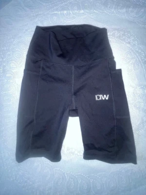 Svarta högmidjade träningsshorts från ICANIWILL - Snygga svarta biker shorts från ICANIWILL med hög midja och praktiska sidofickor. Tillverkade i stretchigt funktionsmaterial som passar perfekt till träning. Logga på ena benet och rynkdetalj bak för extra passform. Aldrig använda