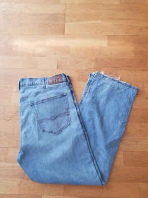 Levi's Denizen - Säljer ett par ljusblå jeans från Denizen Levi's med klassisk femficksdesign och rå kant nertill på benen. Jeansen har en avslappnad passform och är tillverkade i bomullsdenim. Perfekta för en chill och avslappnad stil.
