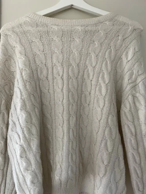 Vit stickad tröja - Säljer en vit kabelstickad tröja med rund hals och långa ärmar. Tröjan har ett flätmönster och går lätt in vid armarna. Jättemysig och söt tröja!!💕