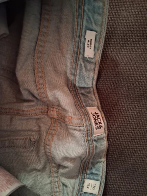 Ljusblå jeans från Jack & Jones - Säljer ett par ljusblå jeans från Jack & Jones med klassisk femficksmodell och raka ben. Jeansen har orange kontrastsömmar och är tillverkade i bomull. Perfekta för en avslappnad och trendig stil.