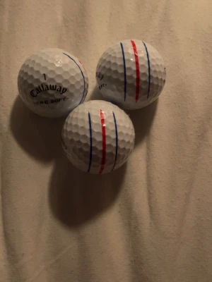 Callaway ERC Soft golfbollar Triple Track - Tre vita golfbollar från Callaway, modell ERC Soft med Triple Track-design. Bollarna har tydliga röda och blå linjer för bättre sikt och precision. Tillverkade i slitstarkt material med klassisk dimple-yta. Perfekta för dig som vill ha extra kontroll på golfbanan.