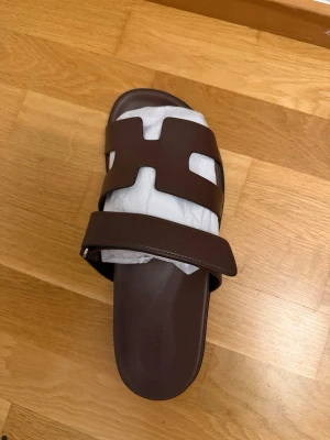  sandaler i läder - Säljer ett par stilrena bruna  sandaler i mjukt läder. Klassisk design med den ikoniska remmen och svart sula. Perfekta för dig som gillar lyxiga och tidlösa detaljer i din outfit.