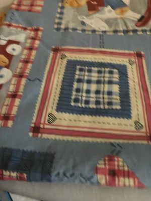 Blått påslakan med nallemönster plus tillhörande örngott - Säljer ett blått påslakan med rutiga och randiga detaljer i rött, vitt och blått samt söta nallebjörnar. Materialet är bomull och mönstret har en lekfull patchwork-stil med hjärtan och rutor. Perfekt för att ge sovrummet en mysig och personlig touch.