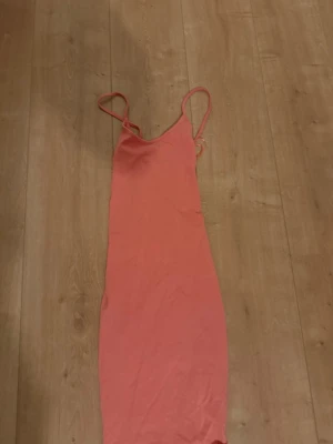 Korallfärgad axelbandslös klänning - Säljer en enkel och snygg korallfärgad klänning med tunna axelband och rak passform. Klänningen är ärmlös och har en slät design utan mönster, perfekt för varma dagar. Materialet känns lätt och passar bra till sommaren.