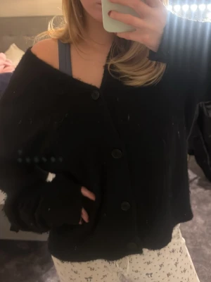 Svart oversized kofta från H&M - Mysig svart kofta från H&M med oversized passform och stora knappar framtill. Koftan har v-ringning, långa ärmar och en lite luddig, mjuk yta.