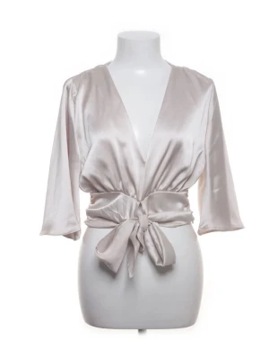 Ljusrosa omlottblus i satin - Snygg ljusrosa omlottblus i glansigt satinmaterial med djup v-ringning och bred knytning i midjan. Blusen har trekvartsärm och en elegant, avslappnad passform som ger en lyxig känsla. Perfekt för att lyfta vilken outfit som helst.