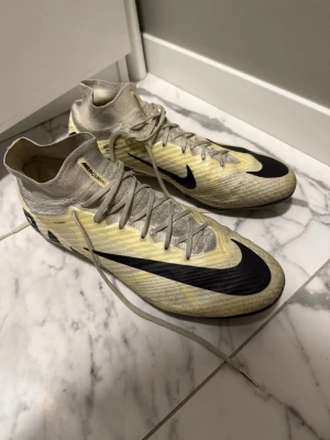 Nike Mercurial gul/svart fotbollsskor - Säljer ett par Nike Mercurial fotbollsskor i gul och svart med högt skaft och snörning. Skorna har en strömlinjeformad design och är tillverkade i lätt syntetmaterial för bästa bollkontroll och snabbhet på planen. Perfekta för dig som vill sticka ut på fotbollsplanen.