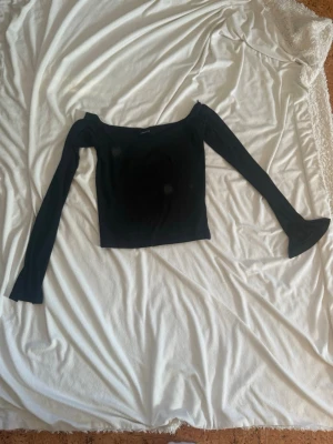 Svart croppad topp med lång ärm - Trendig svart croppad topp med lång ärm och fyrkantig ringning. Perfekt att styla med höga jeans eller kjol för en clean look. Tunn och stretchig kvalitet som sitter snyggt på kroppen.