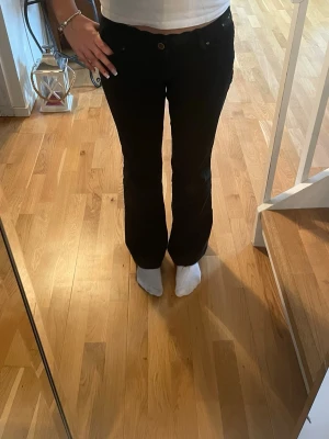 Svarta bootcut jeans - Säljer ett par svarta bootcut jeans med låg midja. Jeansen har en snygg passform som sitter tajt över låren och släpper ut vid bensluten. Perfekta till en trendig vardagslook. Glitter på rumpan och runt midjan. 