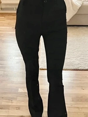 Kostymbyxor från Design by SI  - Snygga svarta kostymbyxor med hög midja och klassisk femficksdesign. Byxorna har en smal passform upptill och lätt utsvängda ben. Perfekta för dig som vill ha en tidlös och trendig look. Storlek xxs. 