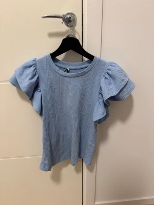 Ljusblå ribbad topp från Zara - Supersöt ljusblå topp från Zara med ribbad struktur och voluminösa korta ärmar. Perfekt för dig som gillar en feminin och trendig stil. Materialet är mjukt och stretchigt, vilket gör den bekväm att bära hela dagen.