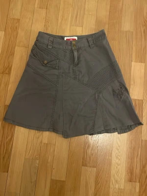Grå kjol y2k från edc vintage - Säljer en grå kjol från edc med coola detaljer som nitar, dekorfickor och synliga sömmar. Kjolen har knappstängning framtill och en unik patchwork-design som ger en edgy känsla. Perfekt för dig som vill ha något annorlunda i garderoben. Y2k och skitsnygg att styla med. Mammas från 2000-talet, har perfekt vintage känsla. Passar xs-s.