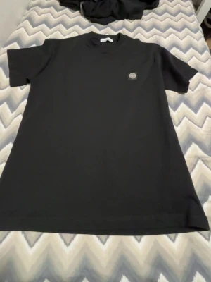 Svart Stone Island t-shirt - Säljer en svart t-shirt från Stone Island med klassisk logopatch på bröstet. T-shirten har rund hals och korta ärmar, tillverkad i mjuk bomull för skön känsla. Enkel och stilren design som passar till det mesta.