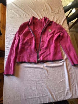 Rosa kofta från New House  - Snygg rosa kofta med grå kantband och knappstängning framtill. Koftan är tillverkad i ett mjukt, strukturerat material. Långärmad och perfekt för lager-på-lager.