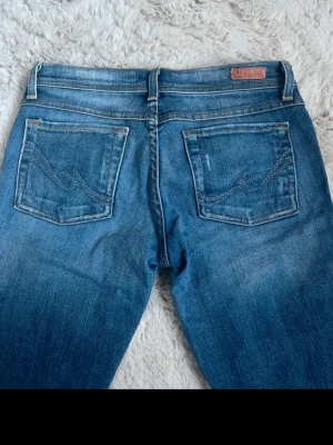 Vintage bootcut jeans - Säljer ett par klassiska blå bootcut jeans  med snygga detaljerade bakfickor och slitningar för en cool look. Jeansen har normal midja och är tillverkade i mjukt denimtyg som sitter skönt. Perfekta för dig som gillar en avslappnad men trendig stil.